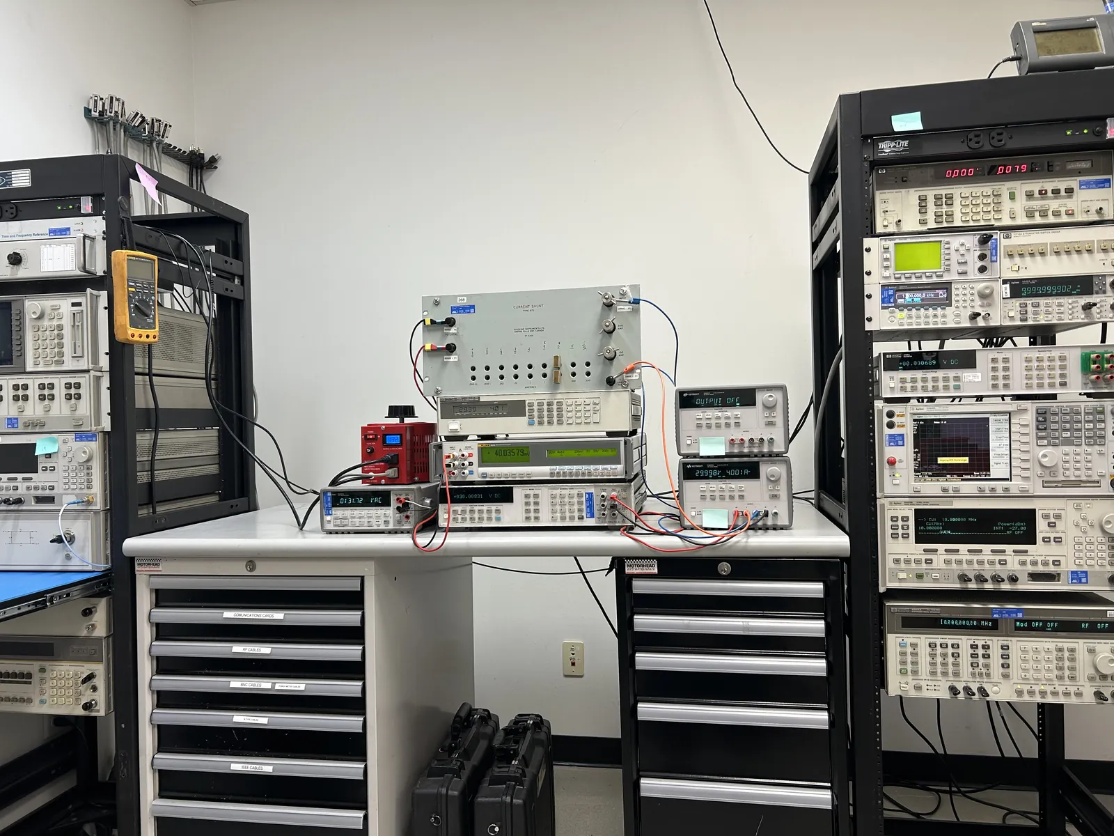 Electrical calibration bench at American Gage with precision multimeters, current shunt, and racks of signal-generation and measurement standards